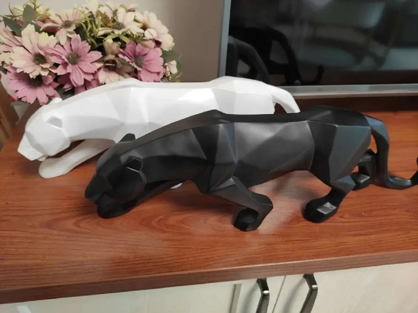 Black and white panther figurines on a wooden surface with flowers in the background