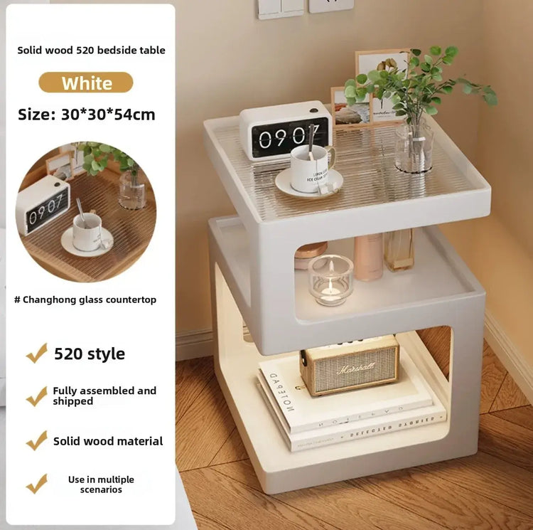 White bedside table with glass top and solid wood base, featuring a clock and cup on the surface. Also has shipping details