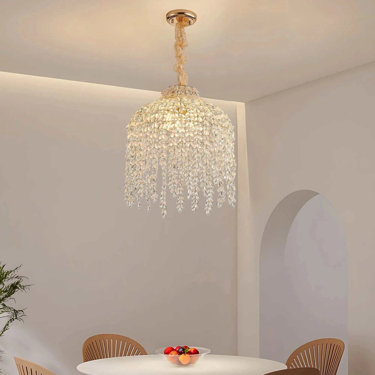 Crystal chandelier hanging above a dining table with fruit bowl and chairs in a room.
