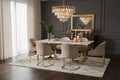 A modern dining table set featuring a rectangular white marble tabletop with a gold metal frame, surrounded by six upholstered dining chairs in beige velvet with matching gold metal legs. The set is styled with a vase of green palm leaves and small tabletop accessories on dark background.  Chandelier overhead and a decorative mirror