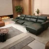 A dark green leather sectional sofa with an extended chaise lounge and reclining center seat, shown in a modern living room setting with a fireplace, rug, and plants.