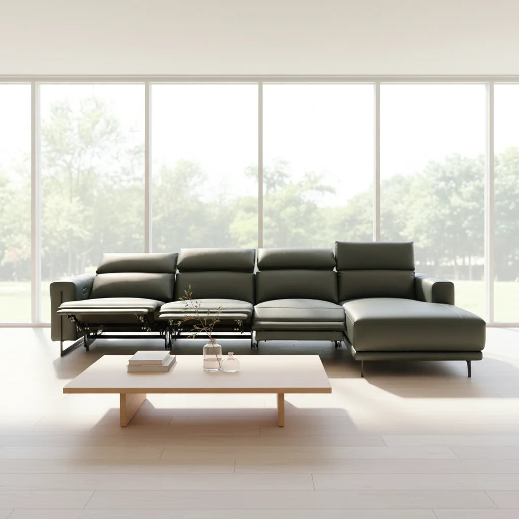 A modern sectional sofa in dark olive green leather, arranged in a bright, minimalist living room with large floor-to-ceiling windows and a light wood coffee table.