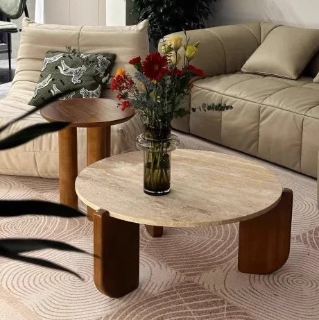 Round wooden coffee table with a vase of flowers in a living room setting.