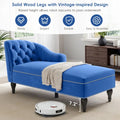 Blue tufted bench with solid wood legs and a robot vacuum cleaner on a carpeted floor.