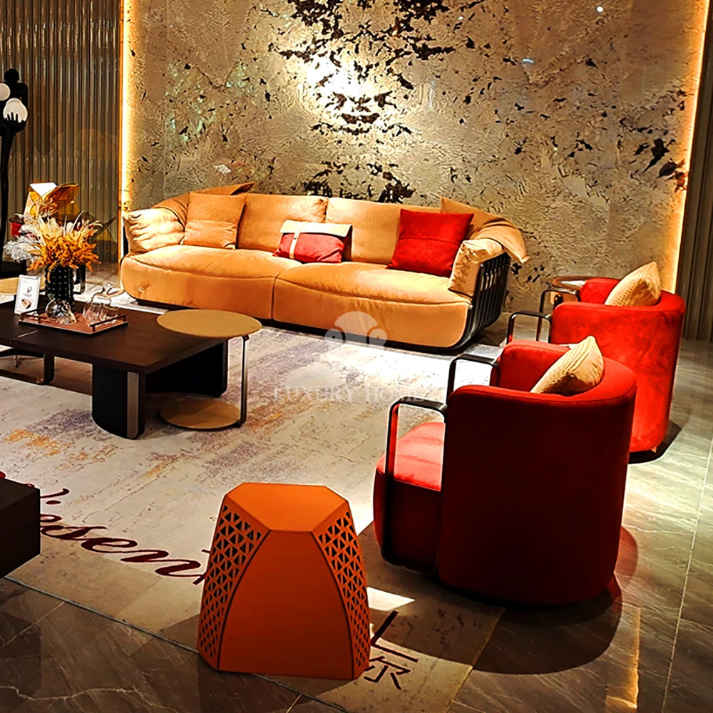 A luxury modern living room setup featuring a large orange velvet sofa, two red armchairs, a dark wood coffee table, and a decorative orange geometric side table on a marble floor.