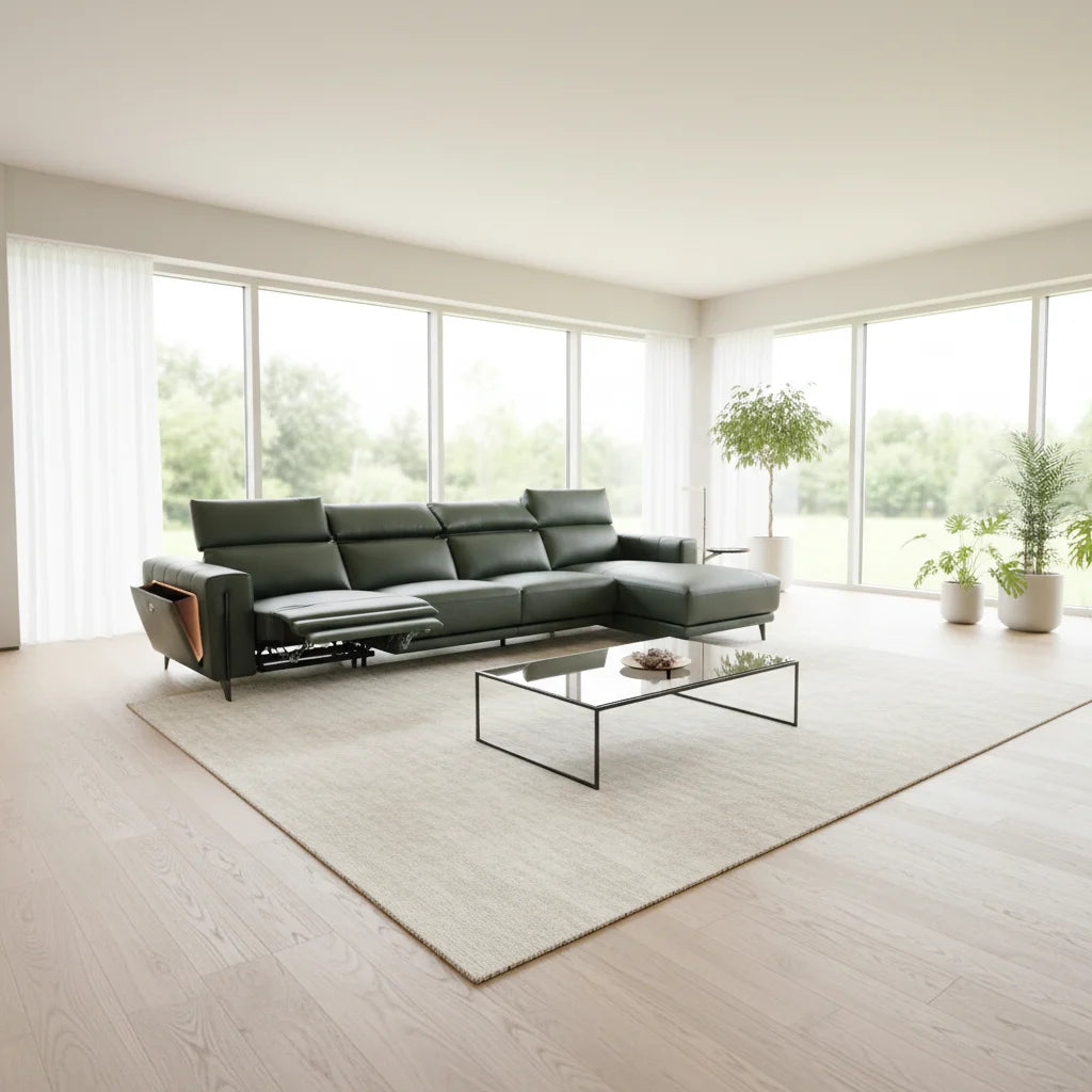 A modern dark green sectional sofa with an extended footrest, styled in a bright, minimalist living room with light wood floors, a beige rug, and large windows.