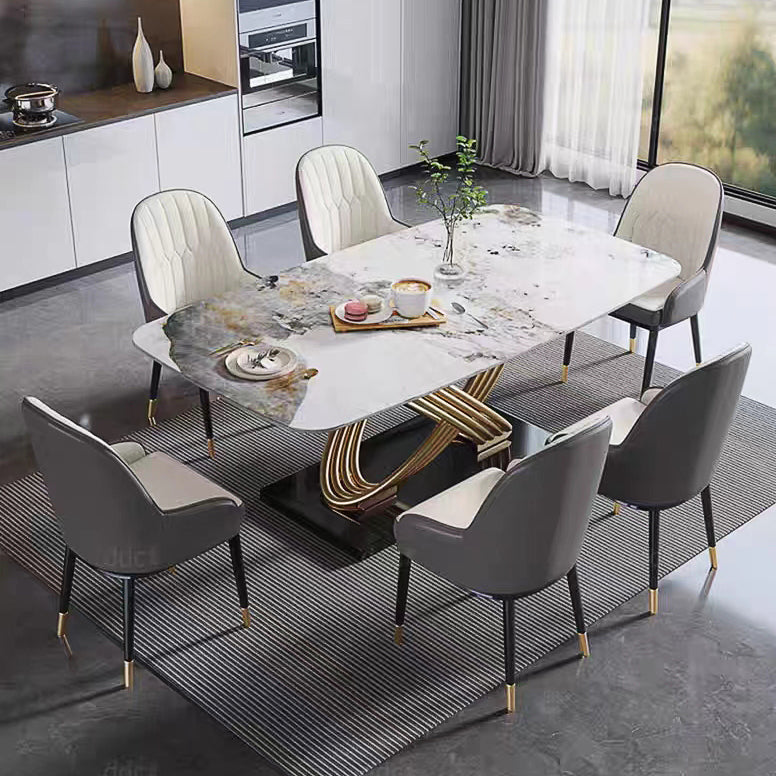 A modern dining room set featuring a rectangular marble-top dining table with a sculptural gold and black base, surrounded by six contemporary gray and cream upholstered chairs on a striped rug.