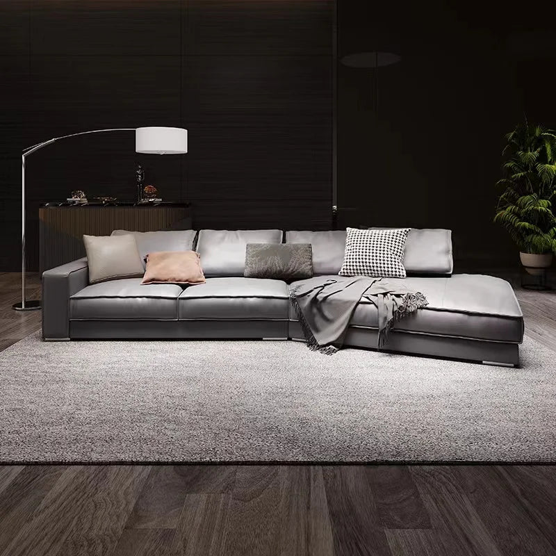 Italian minimalist leather sectional sofa in dark gray with cushions and throw blanket on a rug.