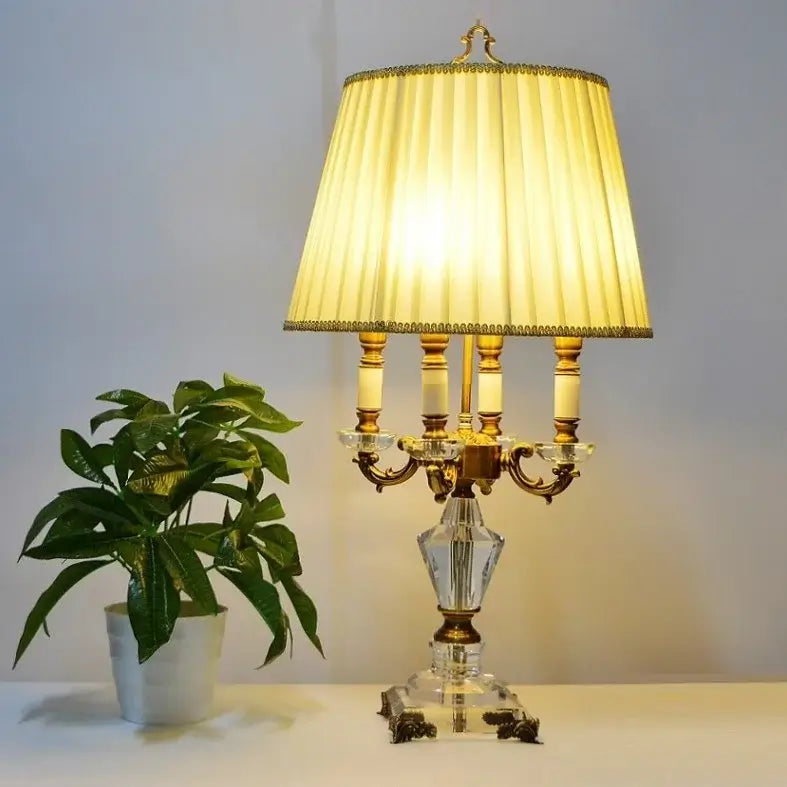 K9 crystal table lamp with fabric shade illuminating a room, accompanied by a green potted plant.