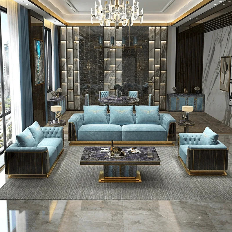 A luxury modern living room set featuring a light blue velvet sofa, two matching armchairs, a small side table, and a marble-top coffee table with gold bases, arranged on a gray rug in a high-end decorated room.