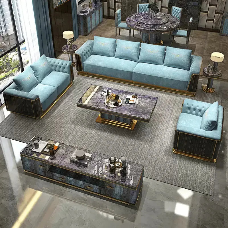 A luxury modern living room furniture set featuring a light blue tufted sofa, two matching armchairs, a marble-top coffee table, and a long media console with gold trim, arranged on a large gray rug in a high-end interior.