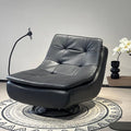 A modern black leather swivel lounge chair with tufted back cushions, shown in a styled interior setting with a patterned rug, a black floor lamp, and a side table with white flowers.