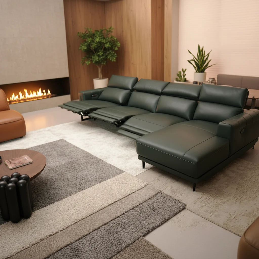 A dark green leather sectional sofa with an extended chaise lounge and reclining center seat, shown in a modern living room setting with a fireplace, rug, and plants.