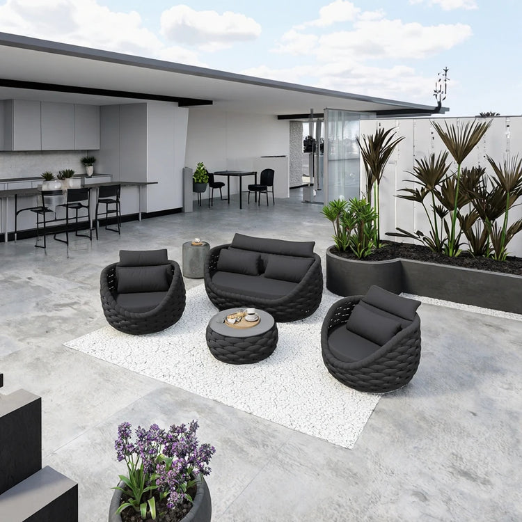 Modern outdoor patio with black furniture, plants, and a building in the background