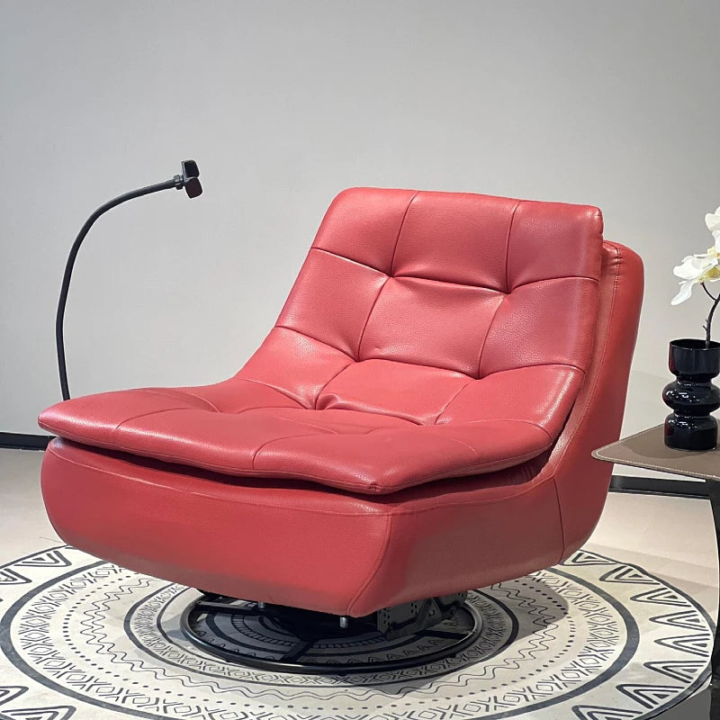 A red tufted leather swivel lounge chair with a low rounded base, shown in a styled interior setting with a black floor lamp, side table, and patterned rug.