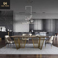 A modern dining room setup featuring a rectangular wooden dining table with distinctive gold metal slatted legs, surrounded by four upholstered dining chairs. The scene is set in a contemporary kitchen with dark cabinets, a geometric tiled backsplash, and a matching geometric area rug.