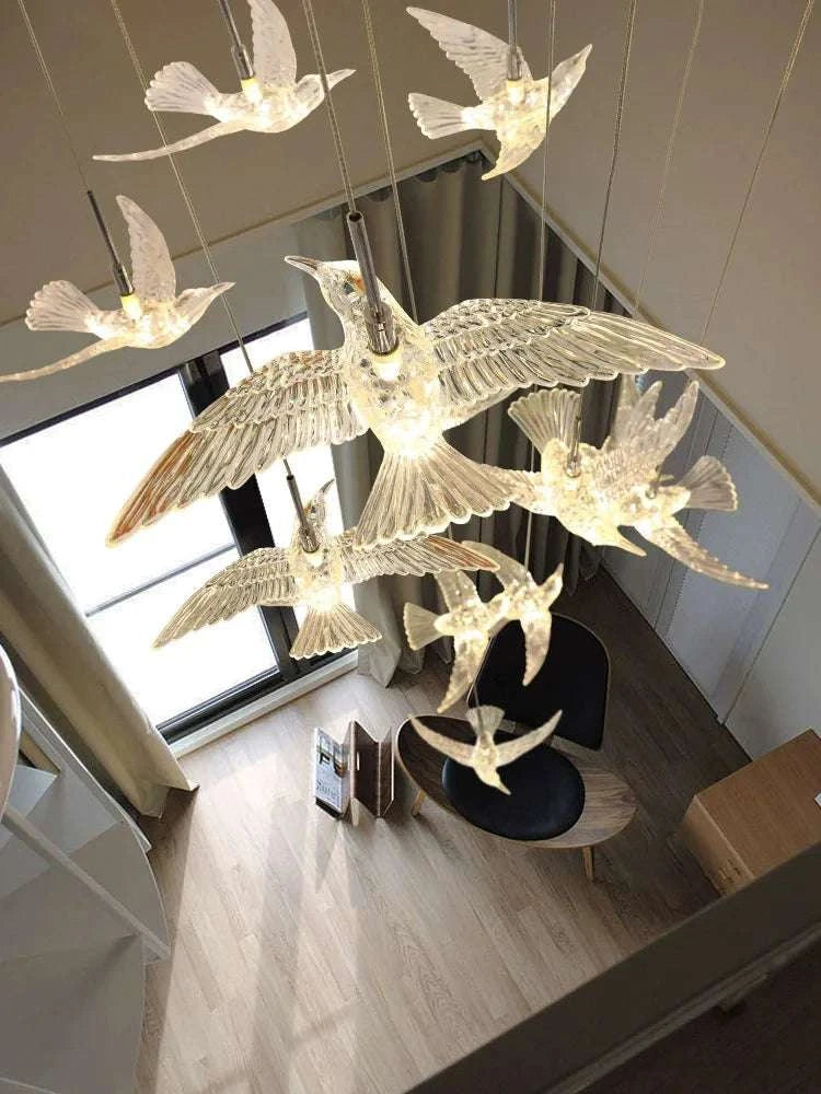 Modern chandelier with bird design in a room with large windows.
