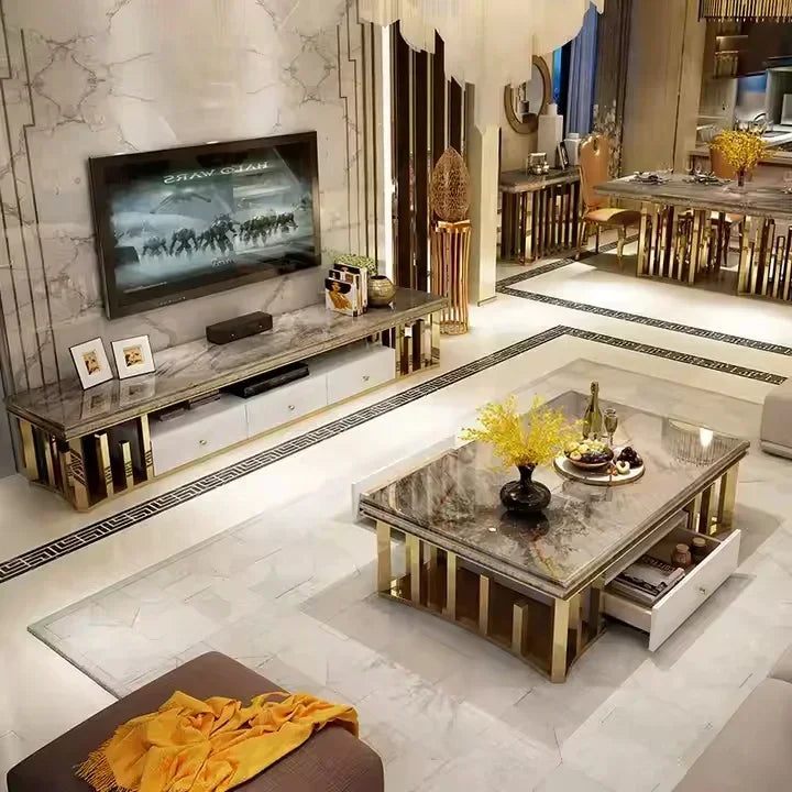 A luxury modern living room featuring a marble TV console and matching coffee table with gold-finished frames and legs, set against a marble wall and a dining area in the background.