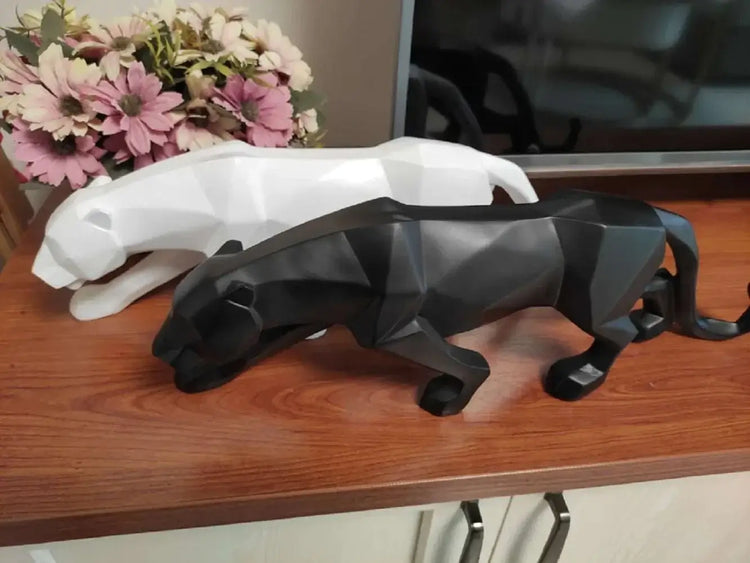 Black and white panther figurines on a wooden surface with flowers in the background