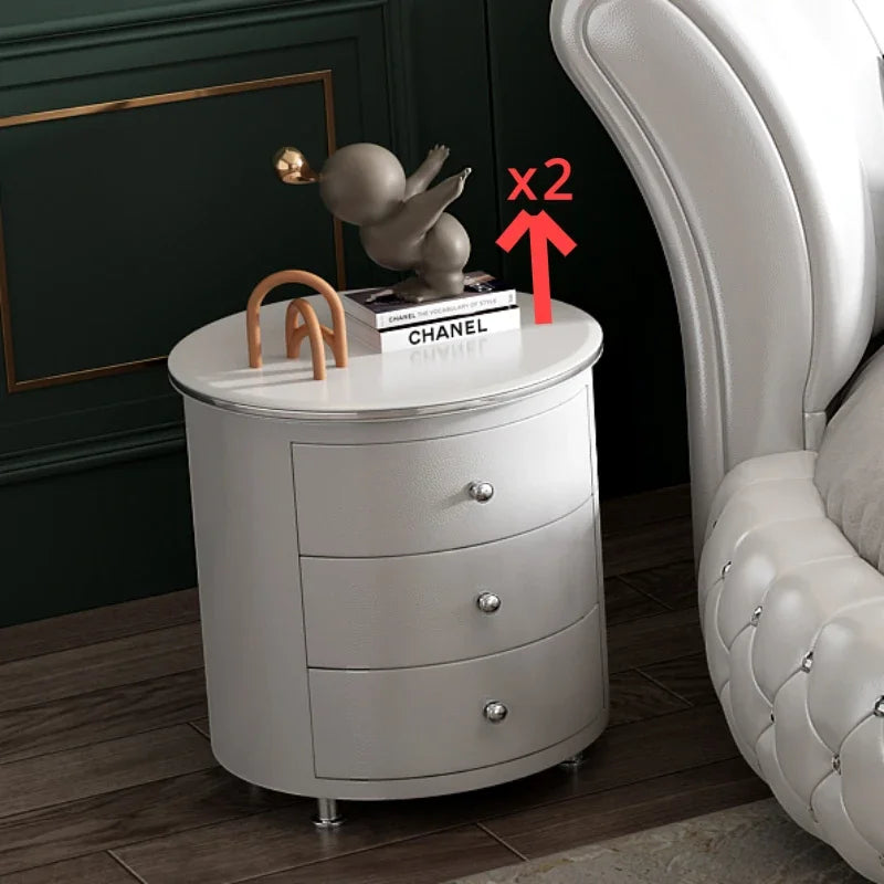 Round gray nightstand with three drawers next to a white upholstered chair.