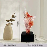Decorative glass sculpture on a black base with measurements, next to a beige vase.