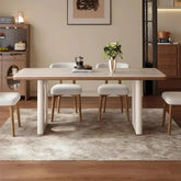 Dining room setup with a table and chairs on a rug, featuring a neutral color scheme.