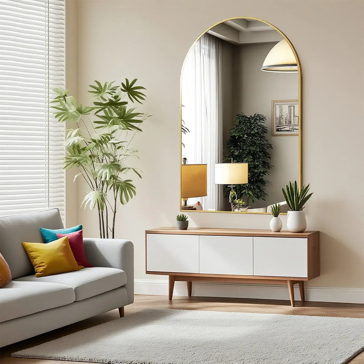 Arched metal framed bathroom mirror hanging above modern console table with plants and decorative items in bright room.