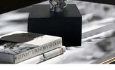 Black cube on a reflective surface with books and a skull decoration.