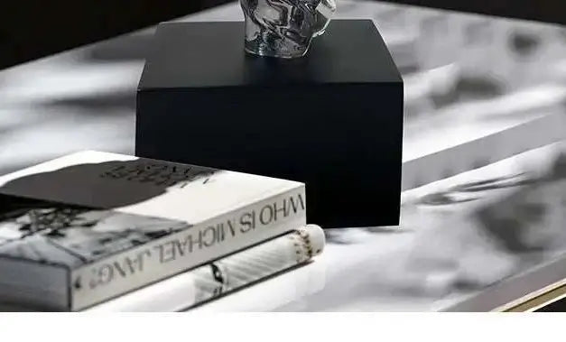 Black cube on a reflective surface with books and a skull decoration.