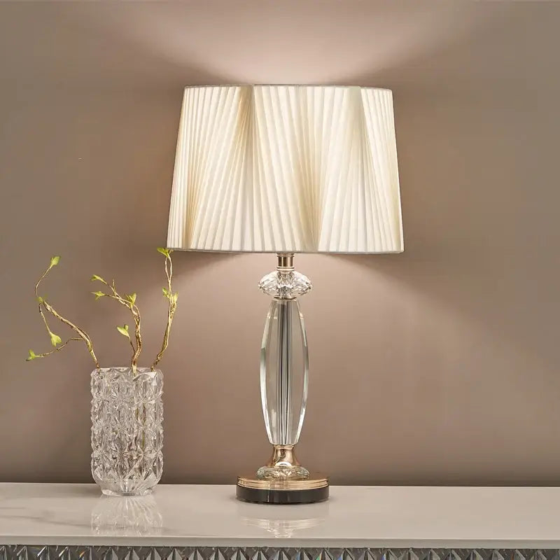 High-end crystal table lamp with fabric shade illuminating a room beside a decorative vase.