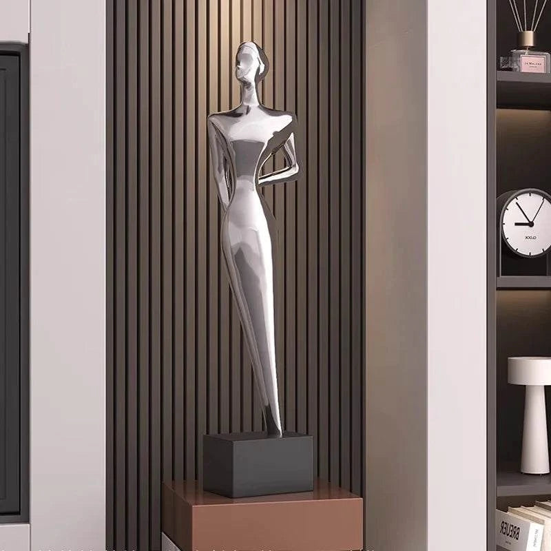 Silver abstract sculpture on a black base in a room setting with a clock and shelves.