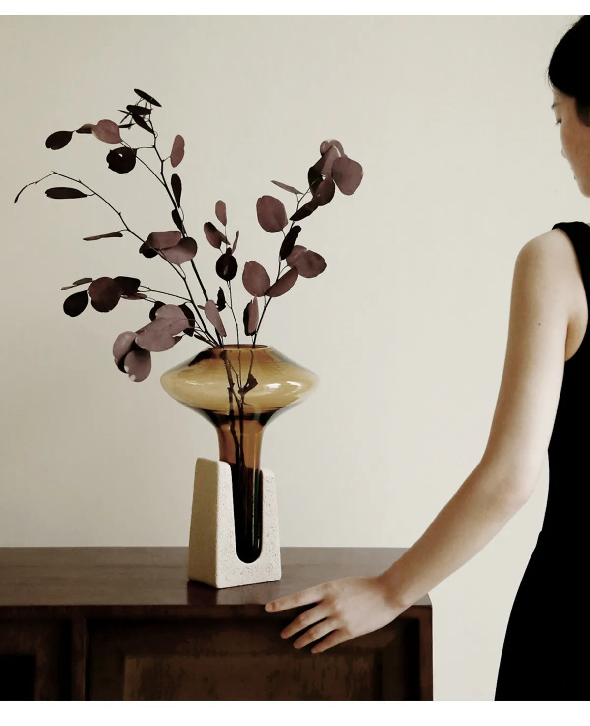 Person interacting with a vase on a table against a plain wall