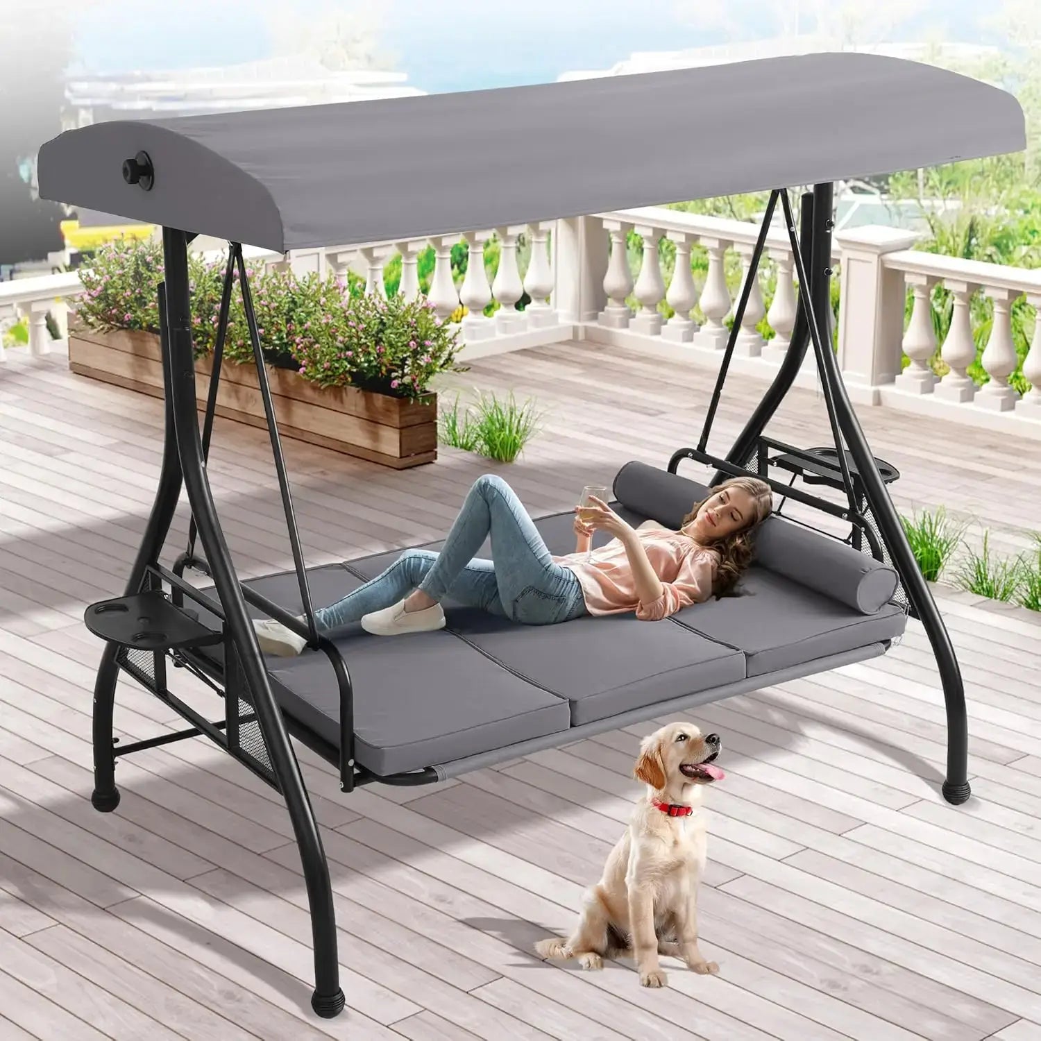 Person lying on a patio swing with a dog sitting on the ground below.