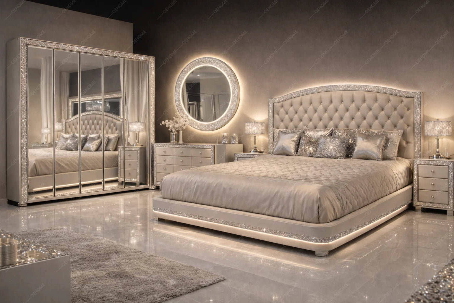 A luxury bedroom set featuring a bed with a tufted, silver-embellished headboard and matching silver nightstands, a large mirrored wardrobe with silver trim, and a glowing round wall mirror against a dark gray wall.