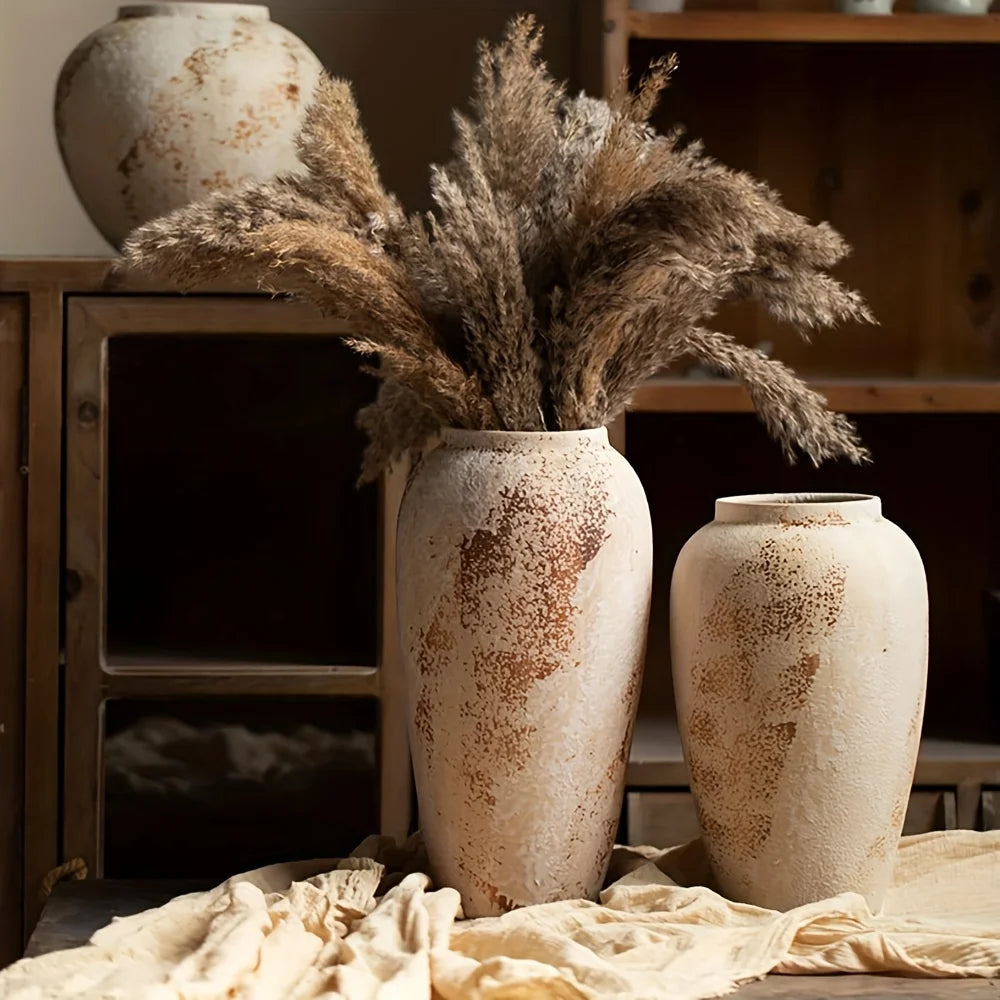 Two rustic vases with dried plants on a wooden surface.