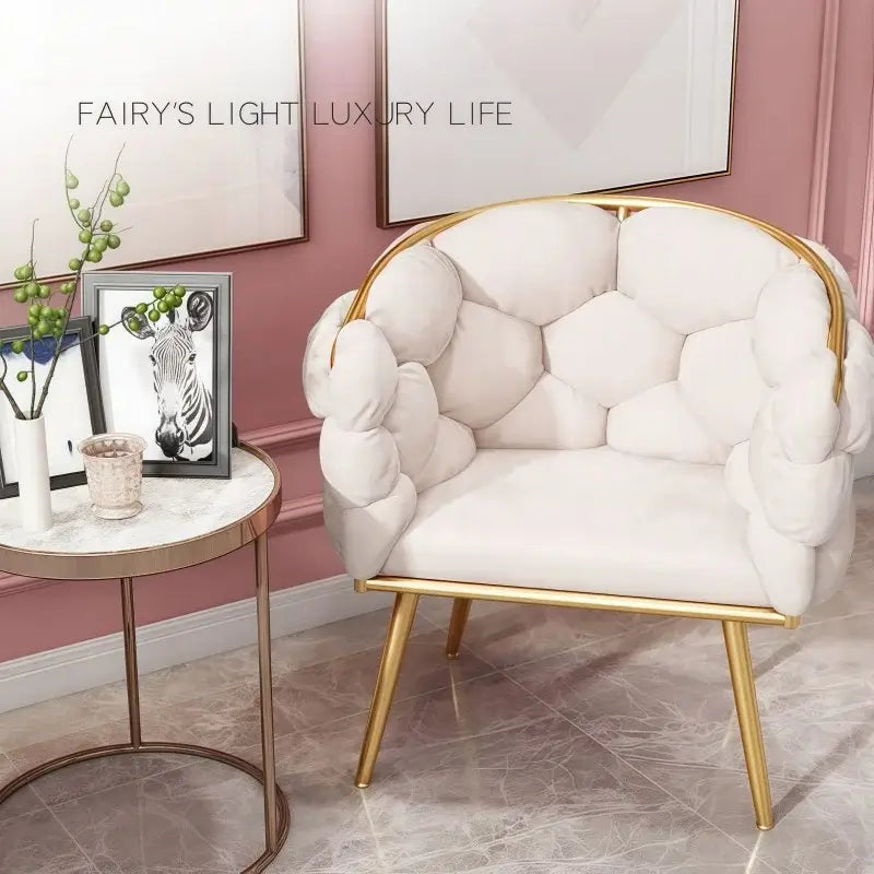 White upholstered chair with gold frame in a room with pink walls and decorative elements.