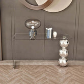 Modern glass console table with decorative items against a gray wall.