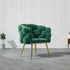 Green velvet armchair with gold legs in a room with white paneled walls and gray floor.
