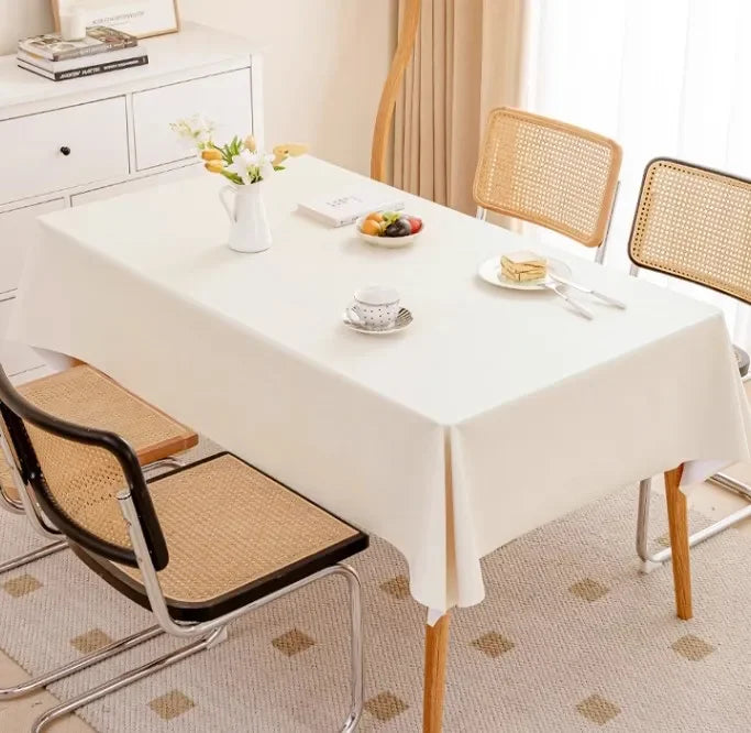 Dining table set with a white tablecloth, chairs, and a small table with books in the background.
