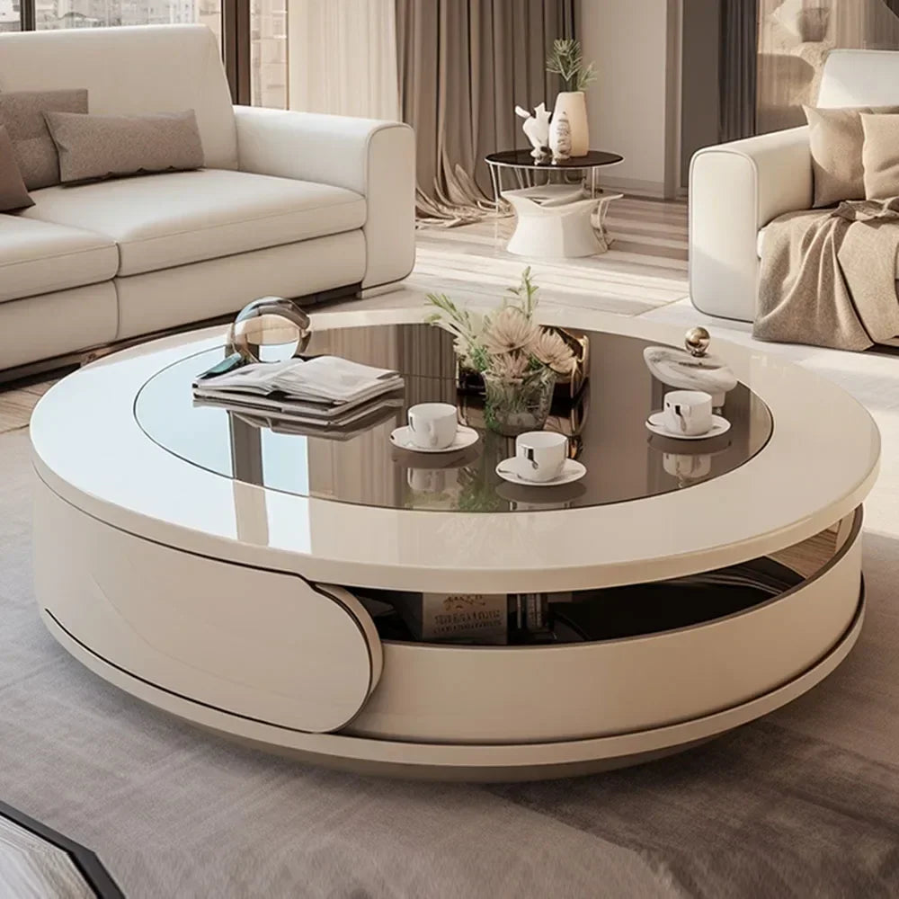A modern round coffee table with a glossy dark glass top and cream-colored base, styled in a contemporary living room with a sofa and armchair in the background.