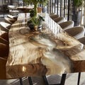 A large live-edge wooden dining table with a glossy resin finish showing natural wood grain and flowing patterns, surrounded by modern upholstered chairs in a bright dining room.