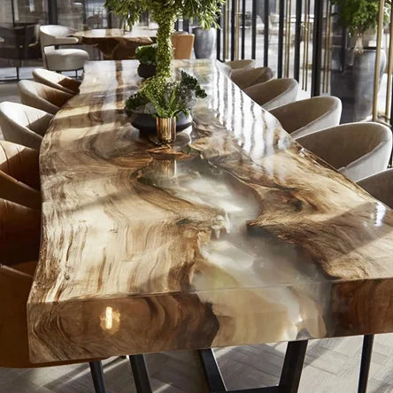A large live-edge wooden dining table with a glossy resin finish showing natural wood grain and flowing patterns, surrounded by modern upholstered chairs in a bright dining room.