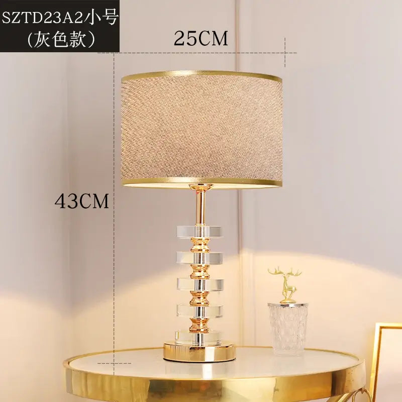 Modern crystal table lamp with fabric shade on a table, featuring a gold base and clear crystal body.
