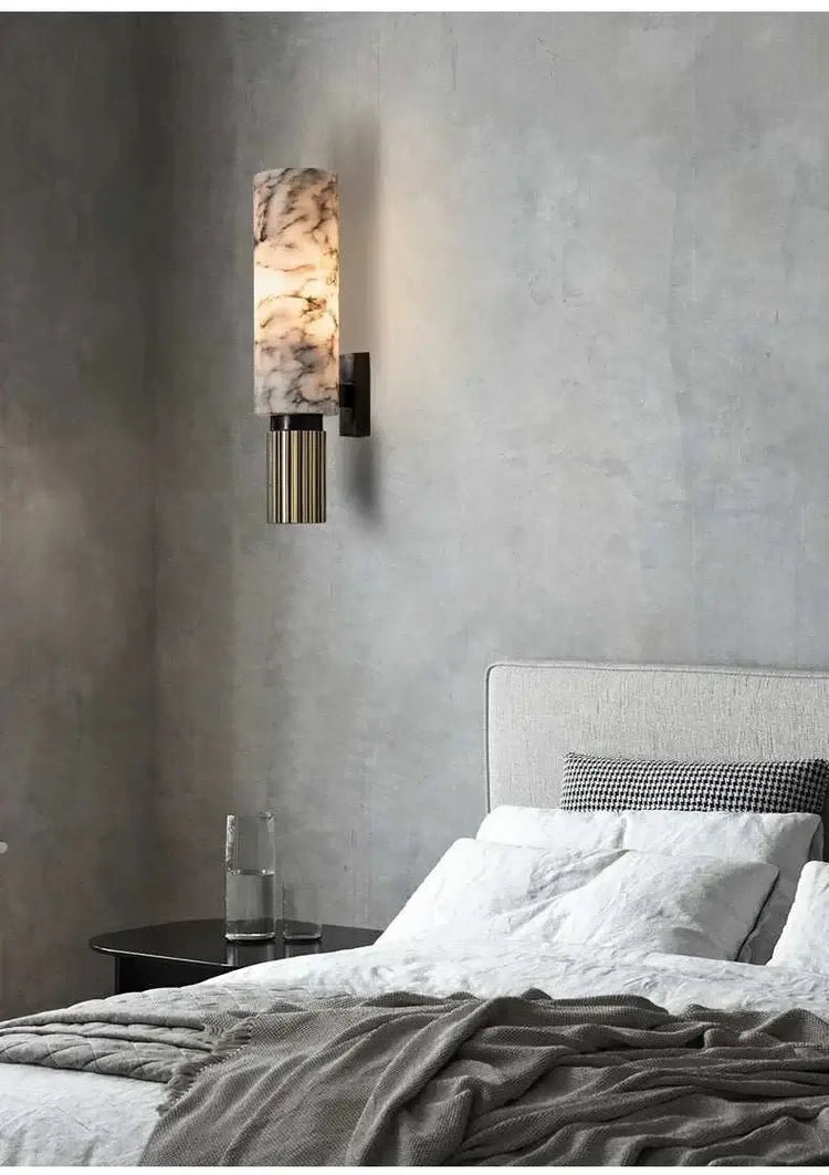 Wall sconce with marble-like finish on a gray wall above a bed.