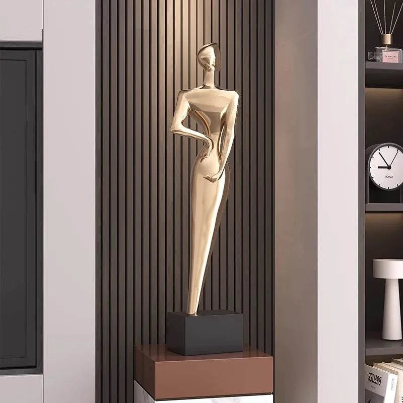 Gold abstract sculpture on a black base against a neutral wall.