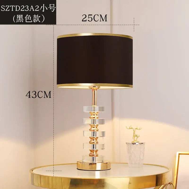 Modern crystal table lamp with fabric shade in black and gold, featuring a clear crystal base, ideal for living spaces.