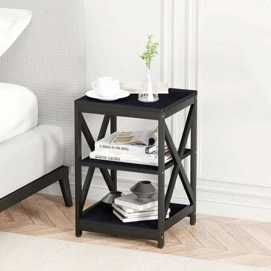 Black side table with books and a plant in a room with a bed and white walls.