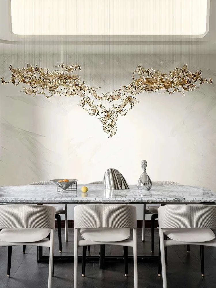 Modern dining room with a large chandelier, marble table, and chairs.
