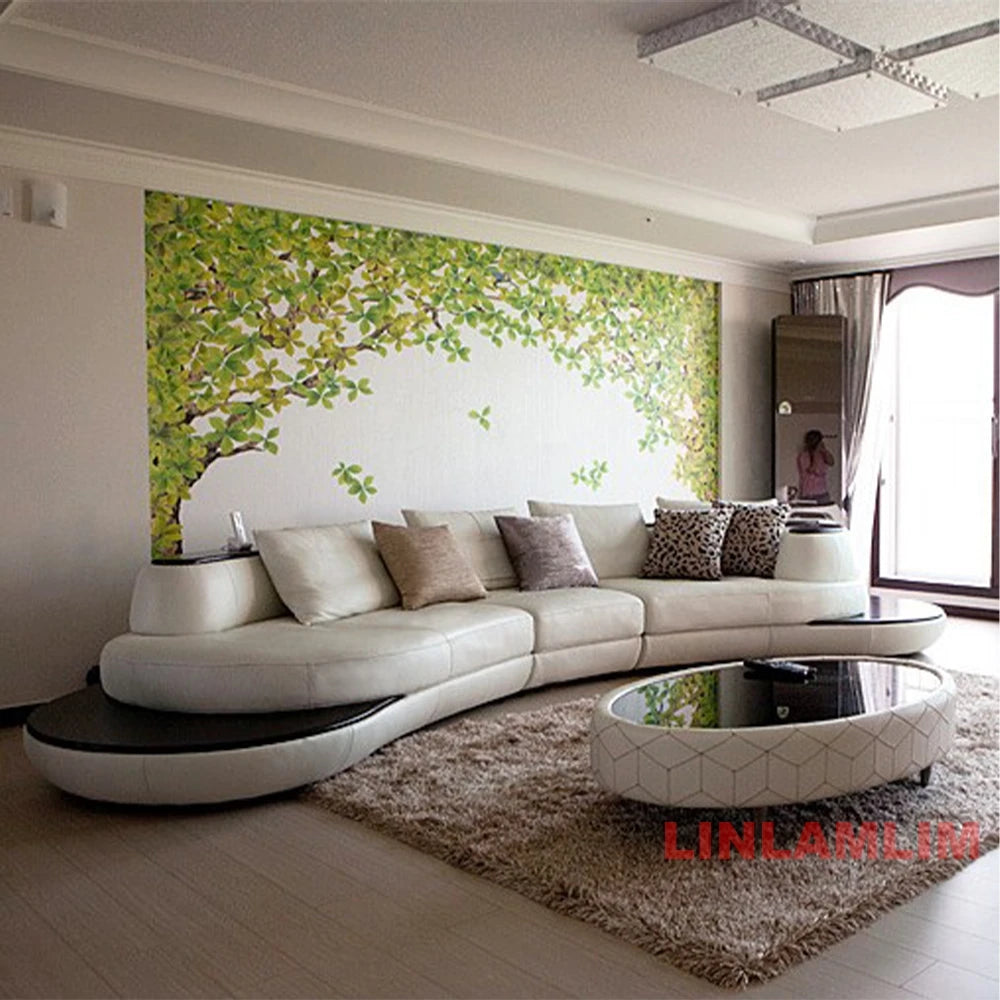 Modern living room with a curved white sofa, decorative pillows, and a large wall mural of green leaves.