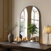 Large arched mirror on a wooden surface with decorative items in a room.